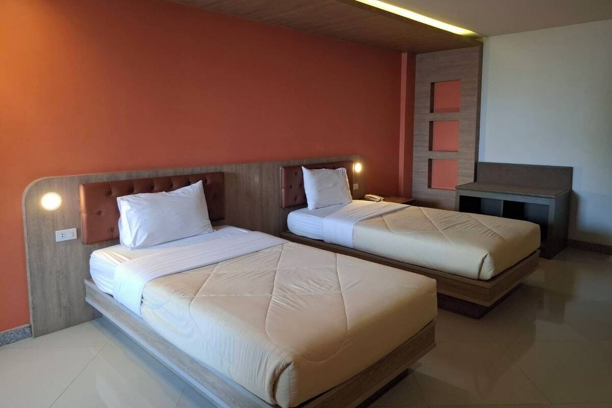 Two single beds with headboards, a small desk, and a wall-mounted shelf unit in a room with orange walls and wooden ceiling.