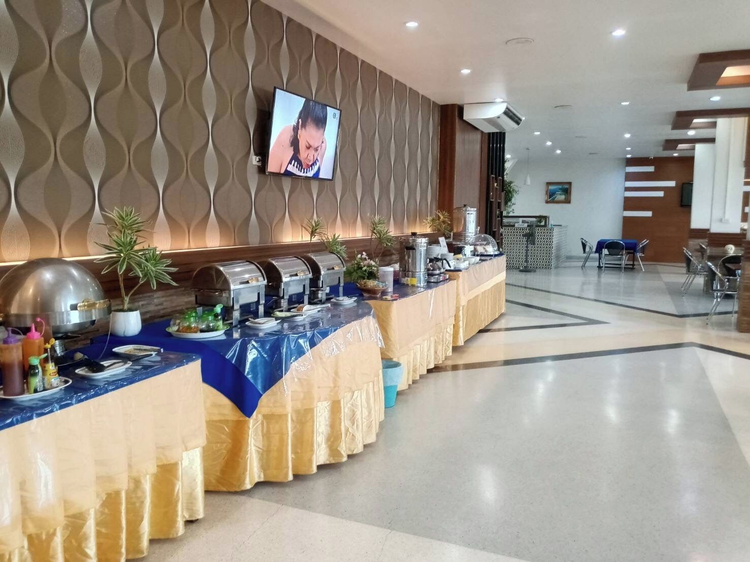 A buffet setup with multiple food stations, a television screen, and a seating area with chairs.