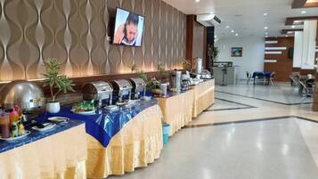 A buffet setup with multiple food stations, a television screen, and a seating area with chairs.