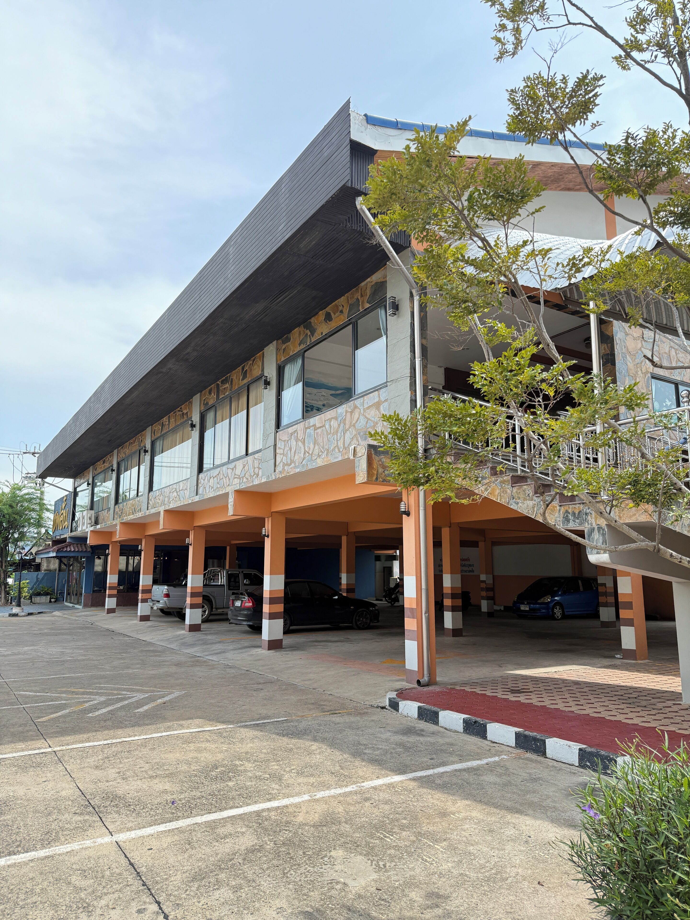 A multi-story building with a covered parking area, large windows, and a stone facade.