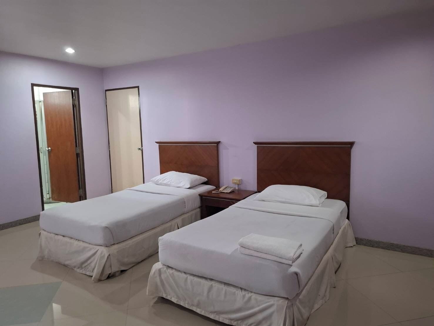 A hotel room with two single beds, a wooden headboard, a bedside table with a phone, and a door.