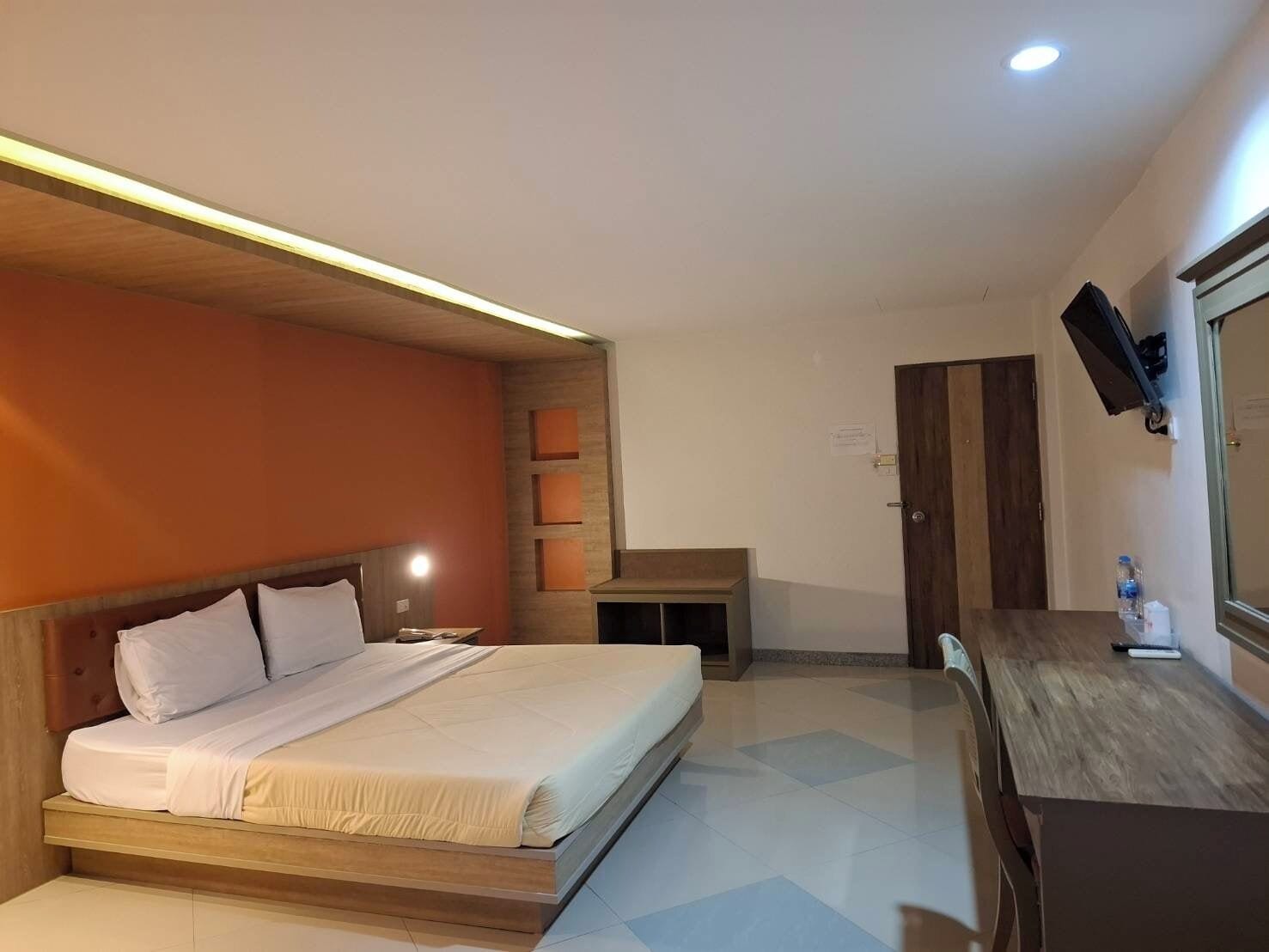 A modern bedroom with a wooden bed, a desk, and a TV mounted on the wall.