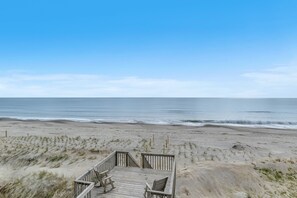 A wooden deck with chairs overlooking a beach with gentle waves.