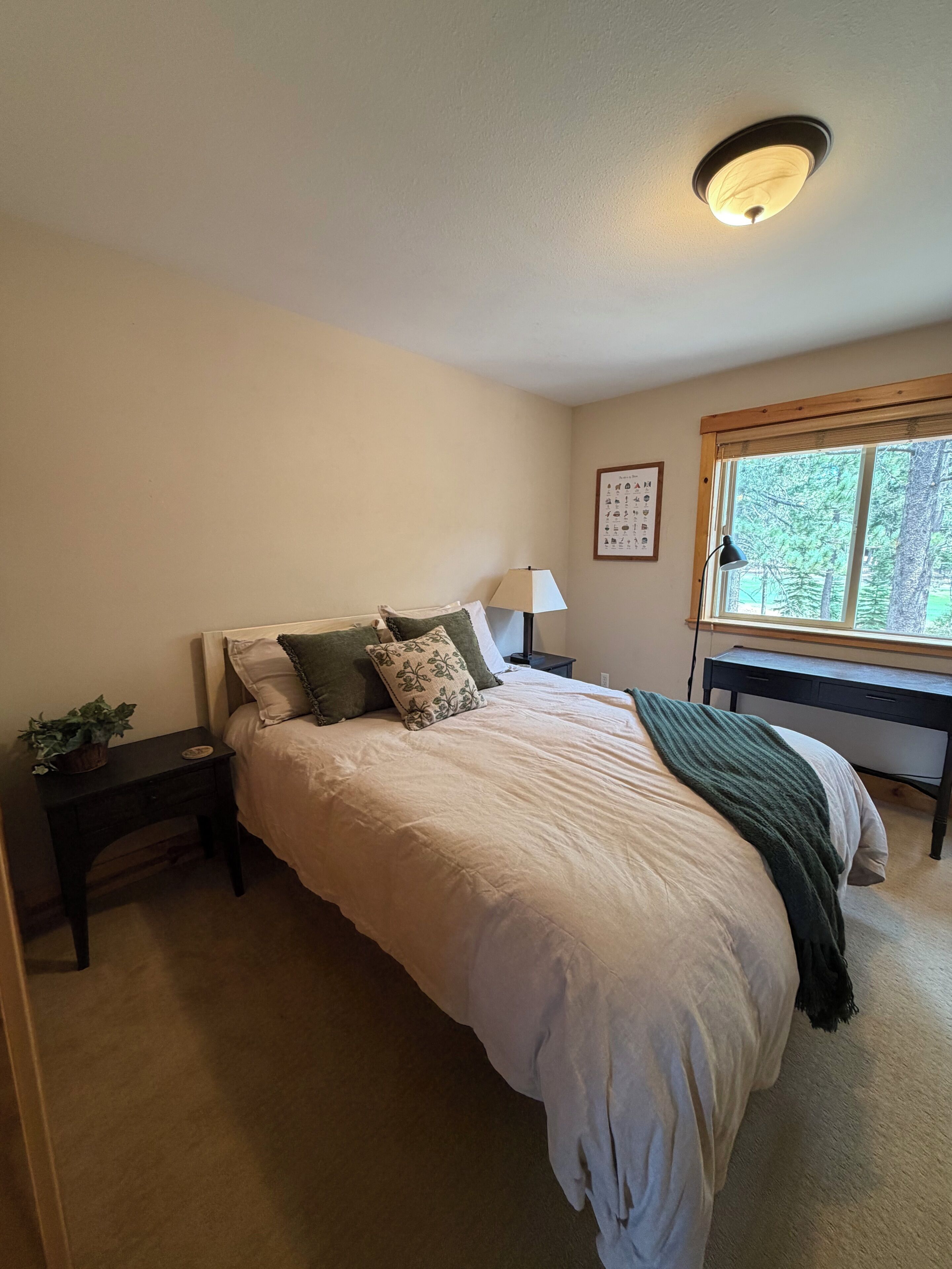 A bedroom with a bed, a nightstand, a lamp, a window, and a ceiling light fixture.