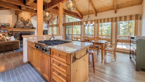 Una cocina amplia con vigas de madera, chimenea de piedra y grandes ventanales.