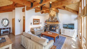 Amplia sala de estar con chimenea de piedra, vigas de madera, televisor grande y un rincón de descanso acogedor.