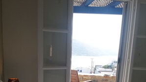 Une chambre à coucher avec un lit, une chaise en bois et une vue sur une plage et des bâtiments, visible à travers une porte ouverte.