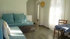Un salon avec un canapé bleu, une petite table recouverte d’une nappe à carreaux et une chaise en bois.