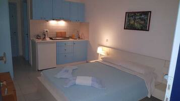 A compact room with a bed, a small kitchenette, and a painting on the wall.