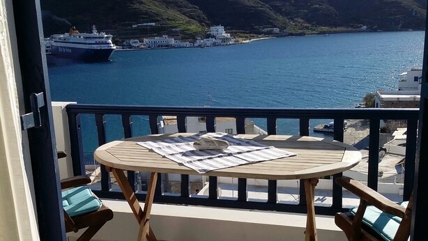 Un balcon avec une table et des chaises, donnant sur une étendue d’eau et un navire au loin.
