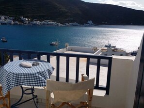 A balcony with a table and chairs overlooking a coastal area with boats and buildings. - Diosmarini Studios & Apartments (Amorgos)