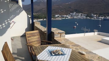 Une terrasse en bois avec une table et des chaises, d’où l’on a vue sur une ville côtière, avec des bateaux et des montagnes en arrière-plan.