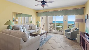 A living room with a beige sofa, a coffee table, and a TV stand. There is a balcony with a view of the ocean. - ⭐Gulf Views | Walk2Beach | Balcony | 2BR Summit at Tops'l 714⭐ (Miramar Beach)