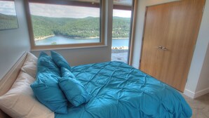 Een slaapkamer met een groot raam dat uitzicht biedt op een bos en een meer.