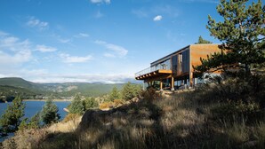 Een modern huis met een balkon met uitzicht op een meer en bergen.