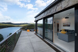 Ein moderner Balkon mit Glasgeländer und Blick auf einen See, mit einer Couch und einem Bild an der Wand.