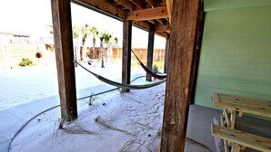 A wooden structure with a hammock, a bench, and a view of palm trees and a building in the background. - Waves, Sand, and Fun in the Sun come join us for a great time. 🌞🍂 (Gulf Shores)