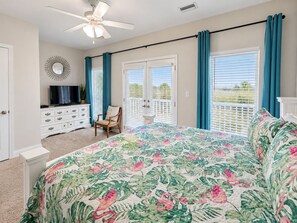 A bedroom with a bed, a television on a dresser, a ceiling fan, and a balcony with curtains. - A Beach Life 3A | 3BR Beach Getaway + Pool (Gulf Shores)