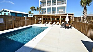A two-story building with a pool, lounge chairs, and a wooden fence. - Waves, Sand, and Fun in the Sun come join us for a great time. 🌞🍂 (Gulf Shores)
