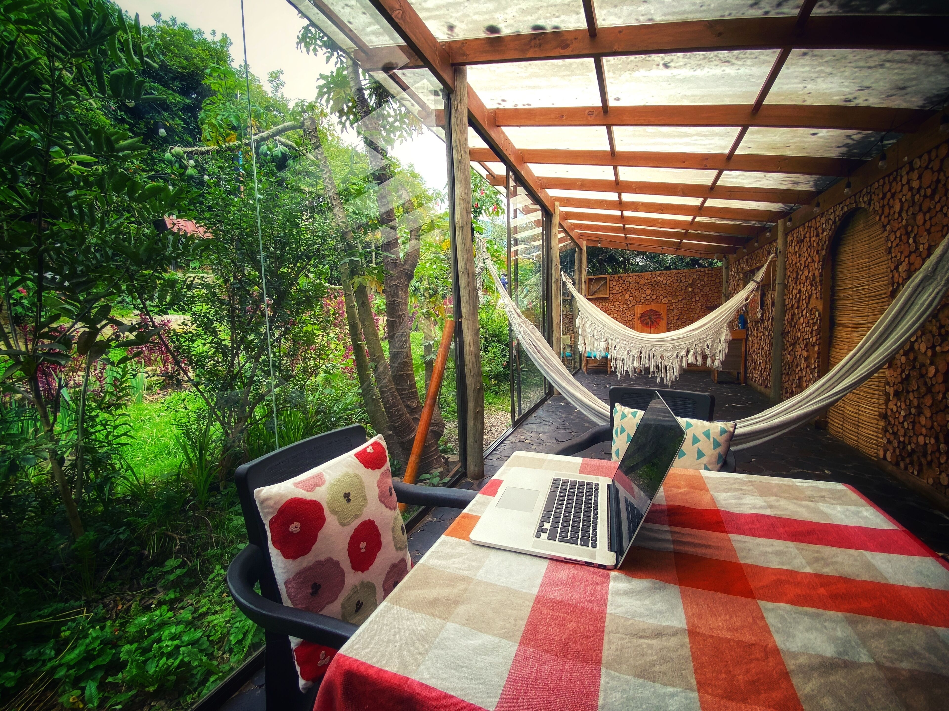 Una hamaca, una computadora portátil y una silla en un espacio exterior cubierto con vistas a vegetación exuberante.