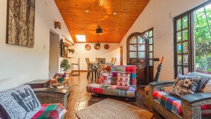 A cozy living room with a high wooden ceiling, a large window, and a comfortable seating area with a sofa and chairs. - Casa Agrreste Bed & Breakfast (Sopó)