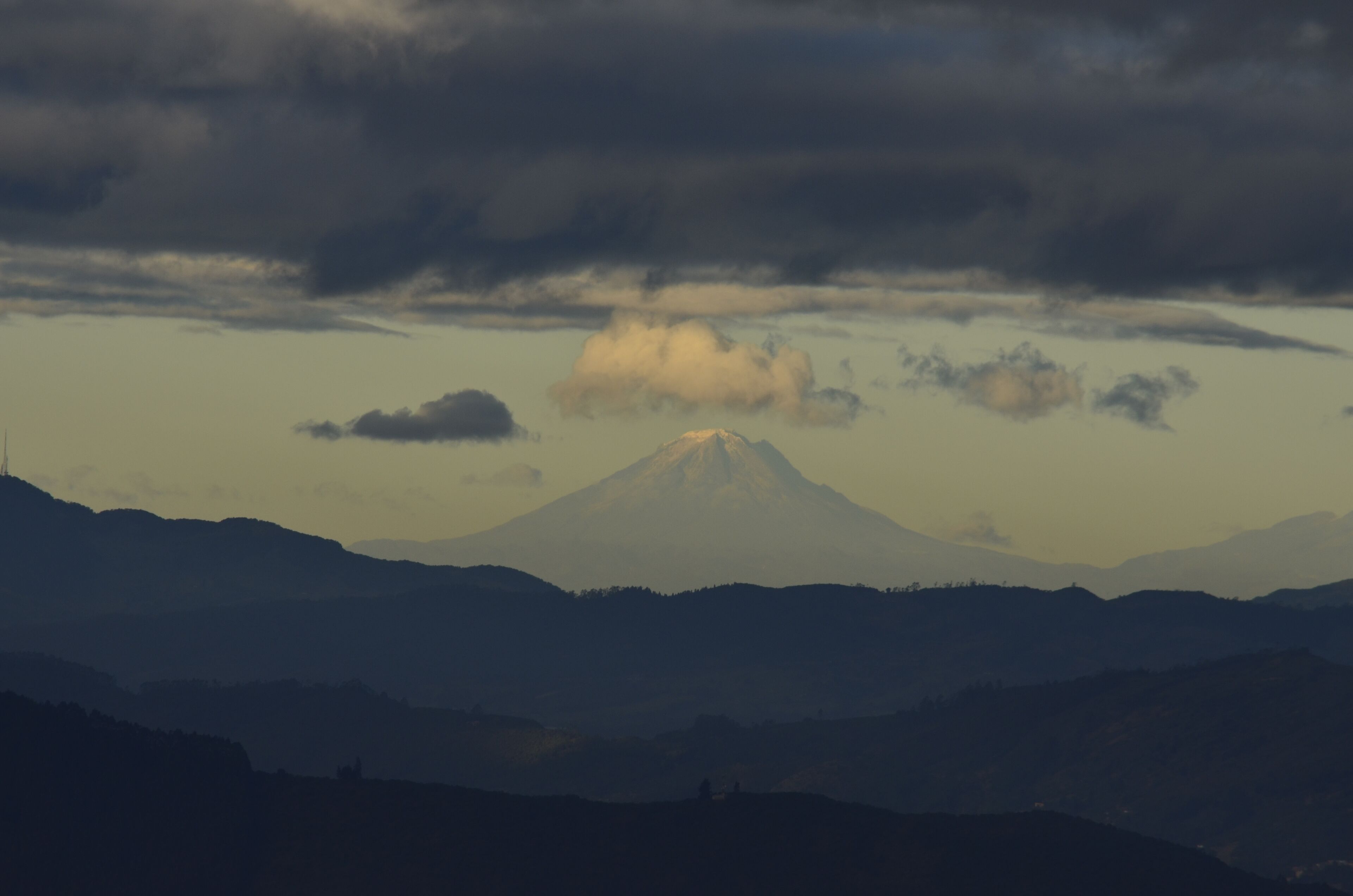 Un paisaje montañoso con un pico destacado, posiblemente un volcán, bajo un cielo nublado.