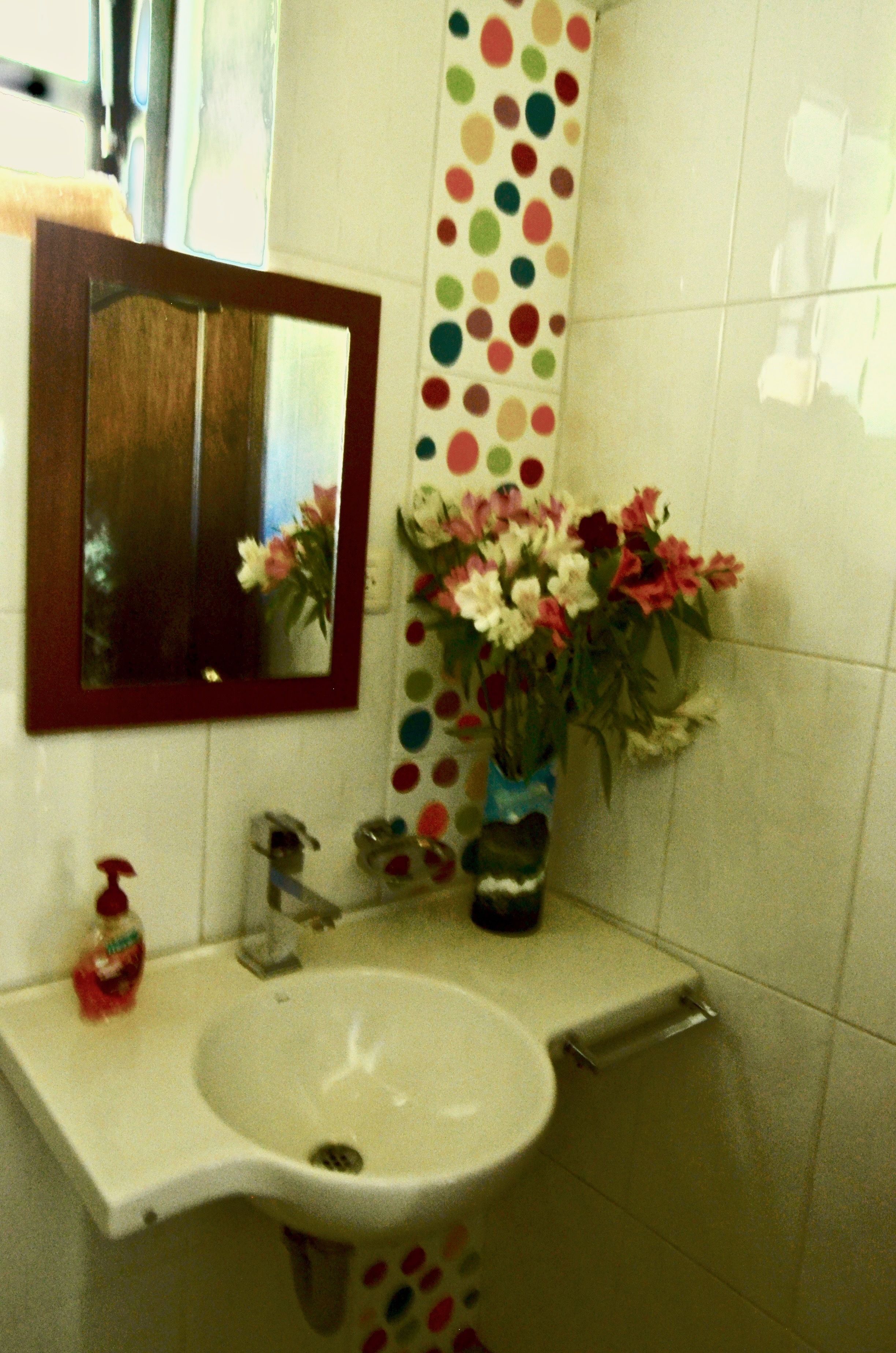 Un baño con un lavabo blanco, un espejo, una toalla de lunares y un florero con flores.