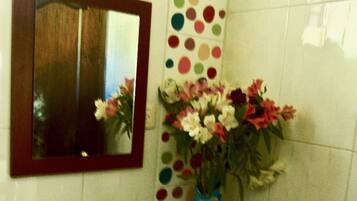 Un baño con un lavabo blanco, un espejo, una toalla de lunares y un florero con flores.