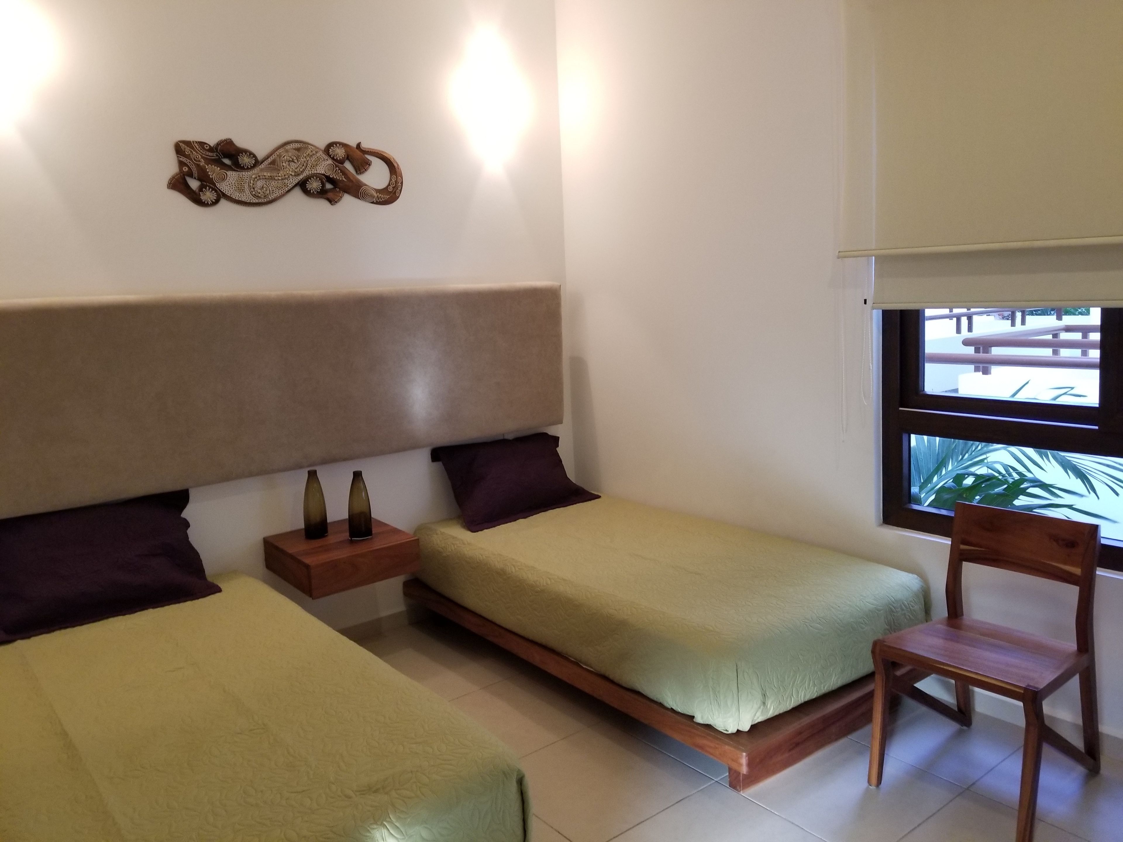 A bedroom with two beds, a nightstand, a chair, and a window with a view of the outside.