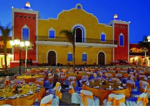 A large outdoor event with tables set up in front of a historic building with a yellow facade and red accents. - TAO Modern Retreat (Akumal)