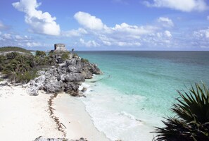 A beach with clear turquoise water, white sand, and a rocky structure with vegetation. - TAO Modern Retreat (Akumal)
