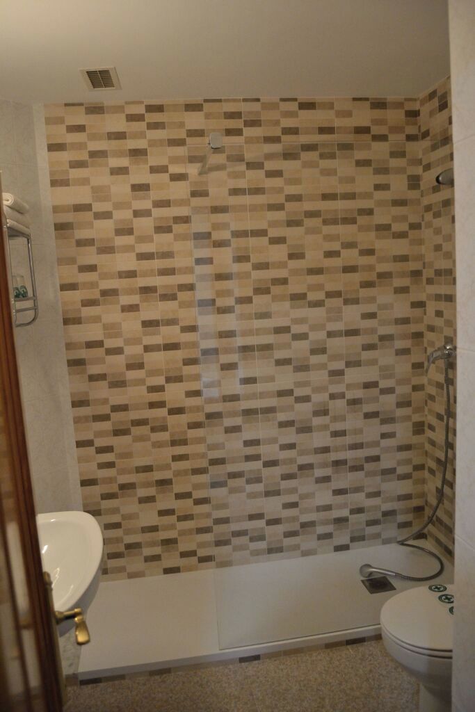 A bathroom with a shower, toilet, and a tiled wall.