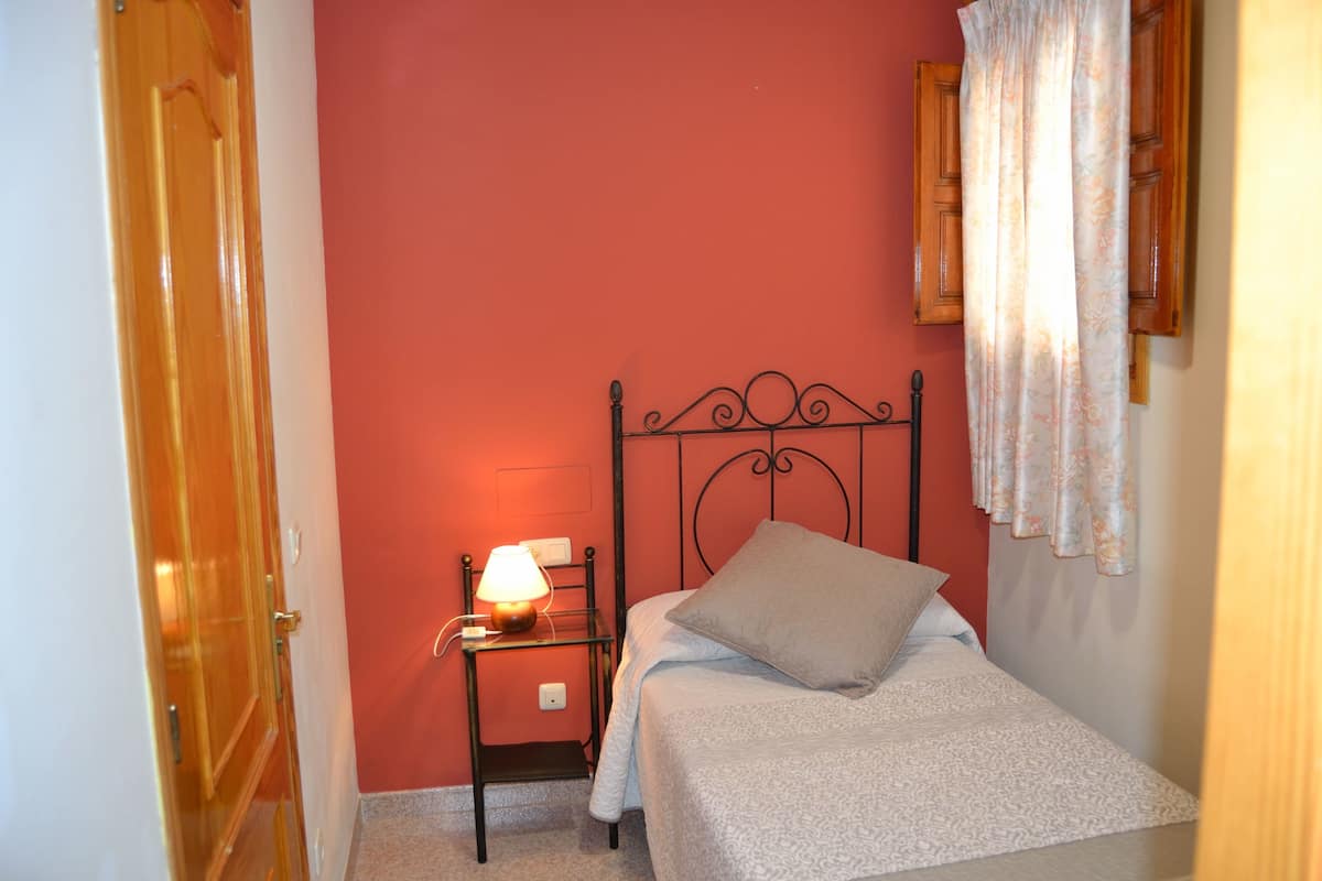 Une chambre à coucher avec un lit, une table de chevet avec une lampe, une porte en bois et un mur rouge.