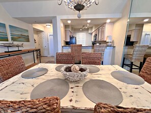 Un coin repas avec une table blanche, des chaises en osier et un lustre.