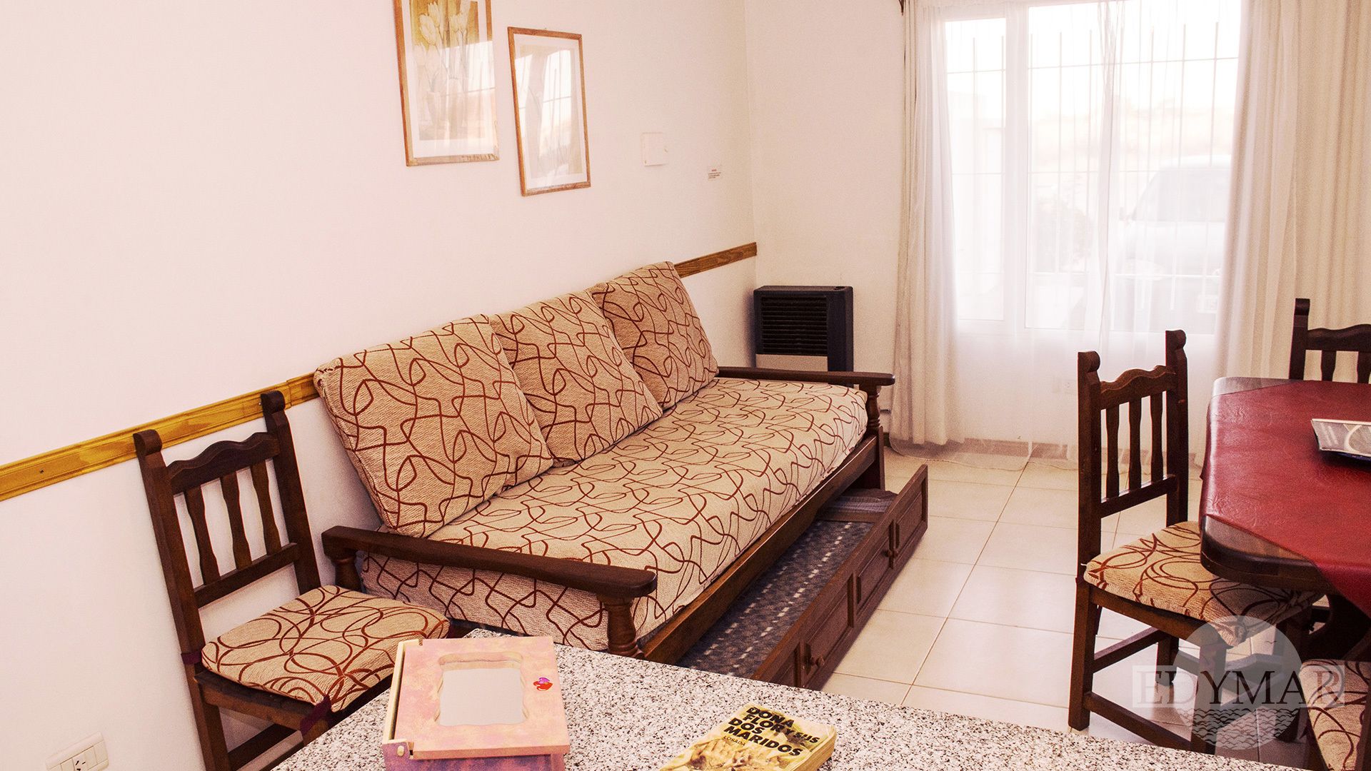 Una sala de estar con un sofá, sillas, una mesita y un ventanal con cortinas.
