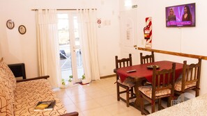 A dining area with a red table and wooden chairs, a sofa with a patterned cover, and a television on the wall. - Edymar (Puerto Madryn)