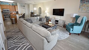 Un salon moderne avec un canapé d’angle, un fauteuil turquoise, une table basse et un téléviseur à écran plat.