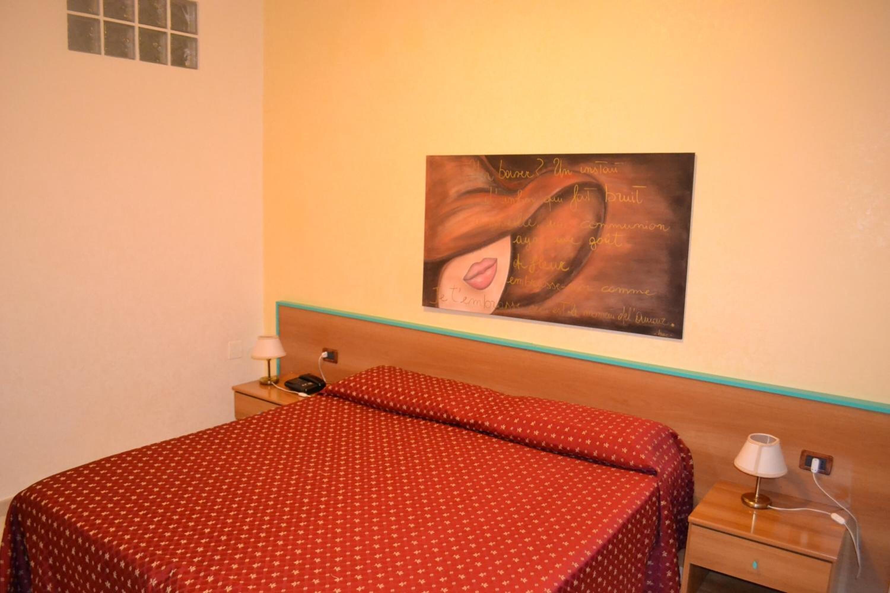 Una habitación de hotel con cama, mesita de noche, lámpara y un cuadro en la pared.