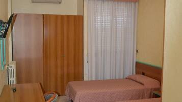 A small, clean room with two single beds, a wooden desk, a chair, and a radiator.