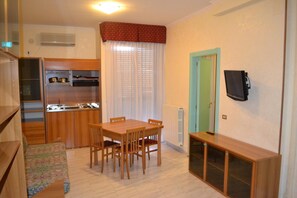 A compact kitchen with a dining table and chairs, a small cabinet, and a TV mounted on the wall. - La Villa dei Gourmets (Foggia)