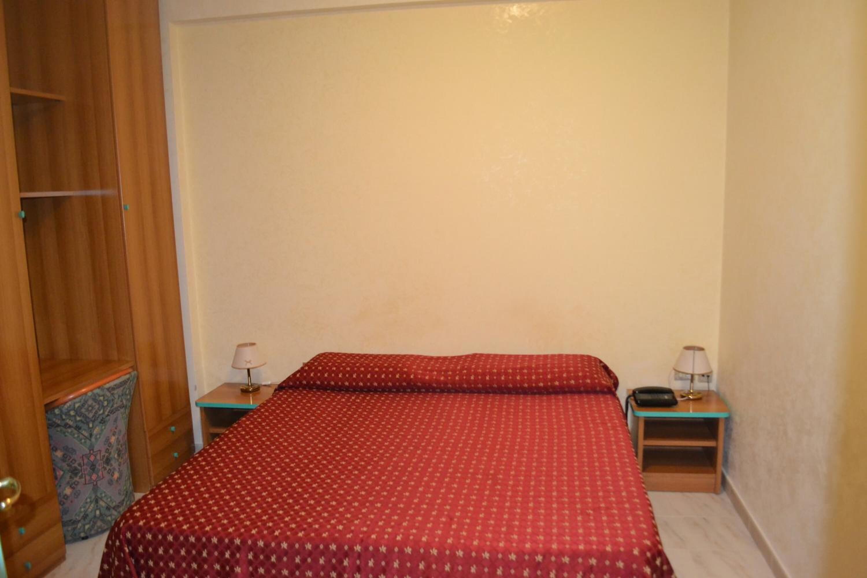 Ein Schlafzimmer mit einem Bett, zwei Nachttischen, einem Kleiderschrank und einem gemusterten Teppich.