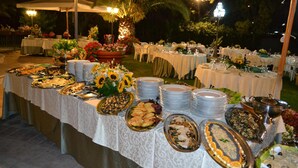 An outdoor buffet setup with multiple tables covered in white tablecloths, featuring various food dishes and a large floral centerpiece. - La Villa dei Gourmets (Foggia)