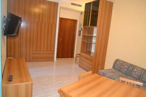 A room with a wooden wardrobe, a television mounted on the wall, a sofa, and a wooden table. - La Villa dei Gourmets (Foggia)