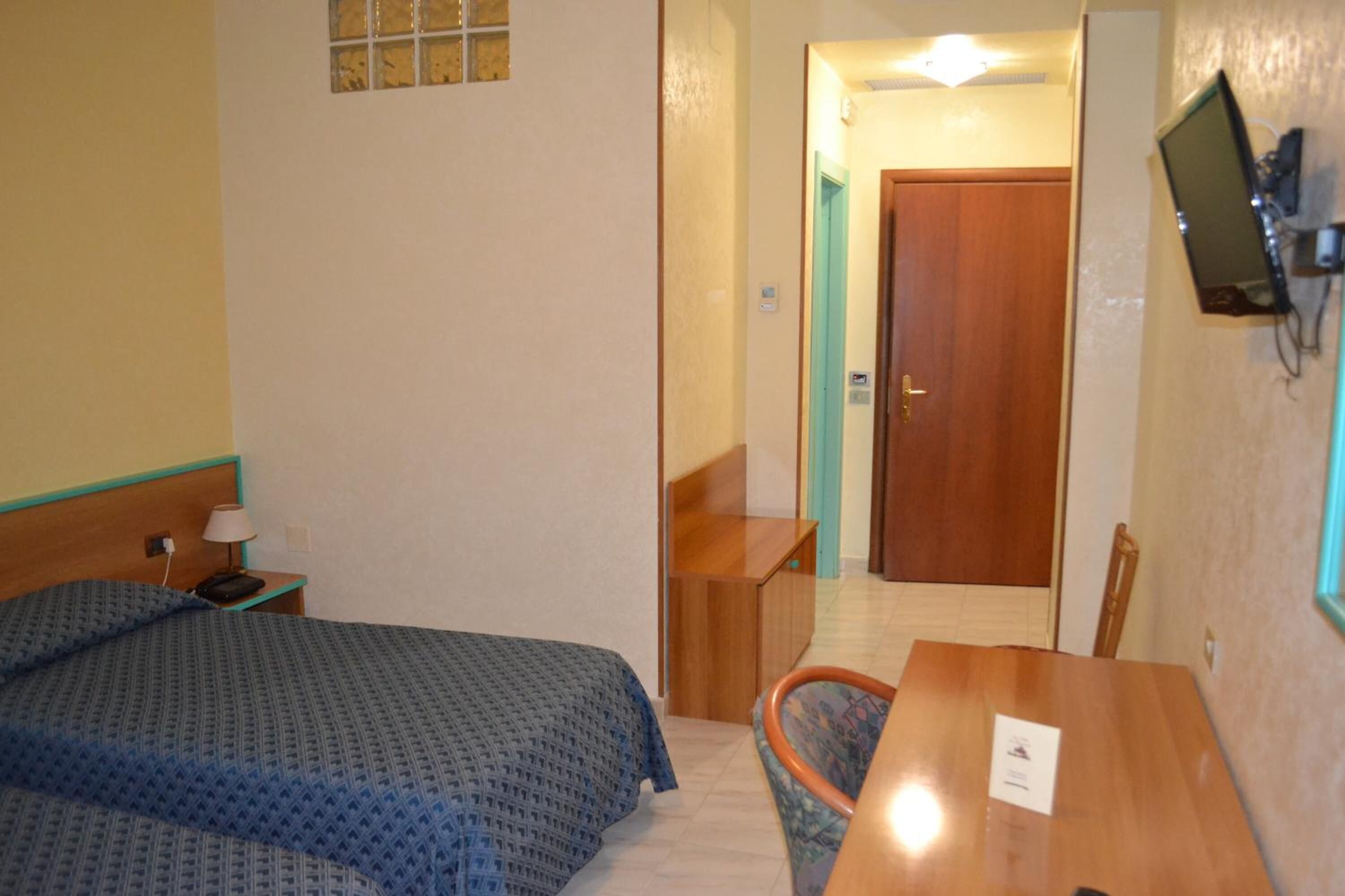 A hotel room with a bed, a desk, a chair, and a TV mounted on the wall.
