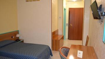 A hotel room with a bed, a desk, a chair, and a TV mounted on the wall.