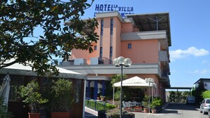 A hotel with a prominent sign, outdoor seating, and potted plants. - La Villa dei Gourmets (Foggia)
