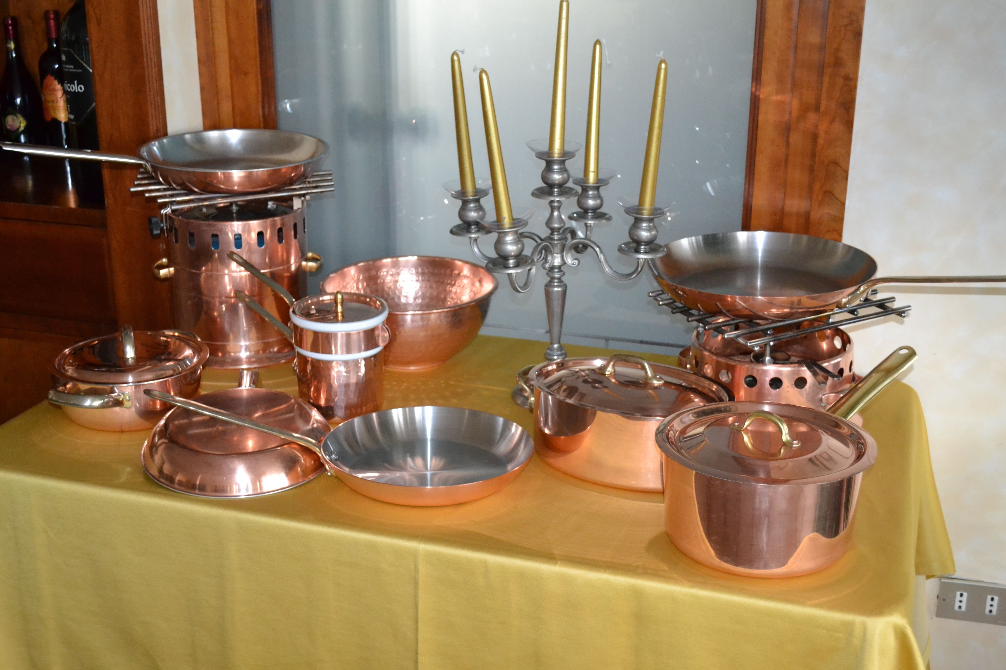 Una mesa con diversos utensilios de cocina de cobre, incluyendo ollas, sartenes y un candelabro.