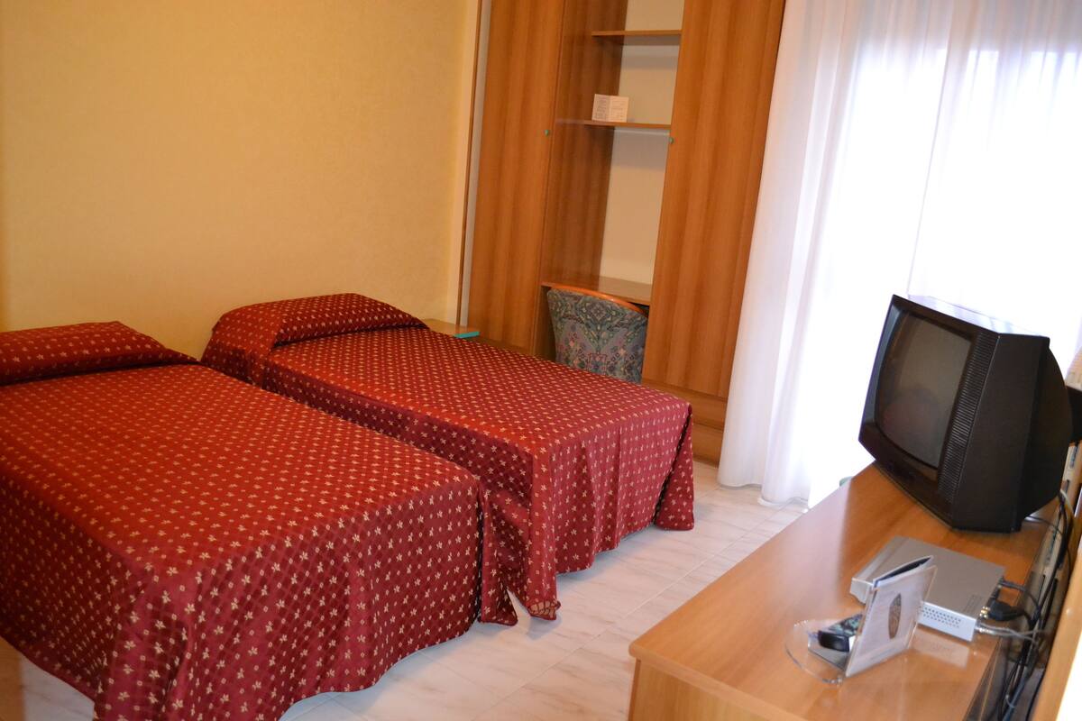 A hotel room with two beds, a TV, and a desk with a computer and phone.