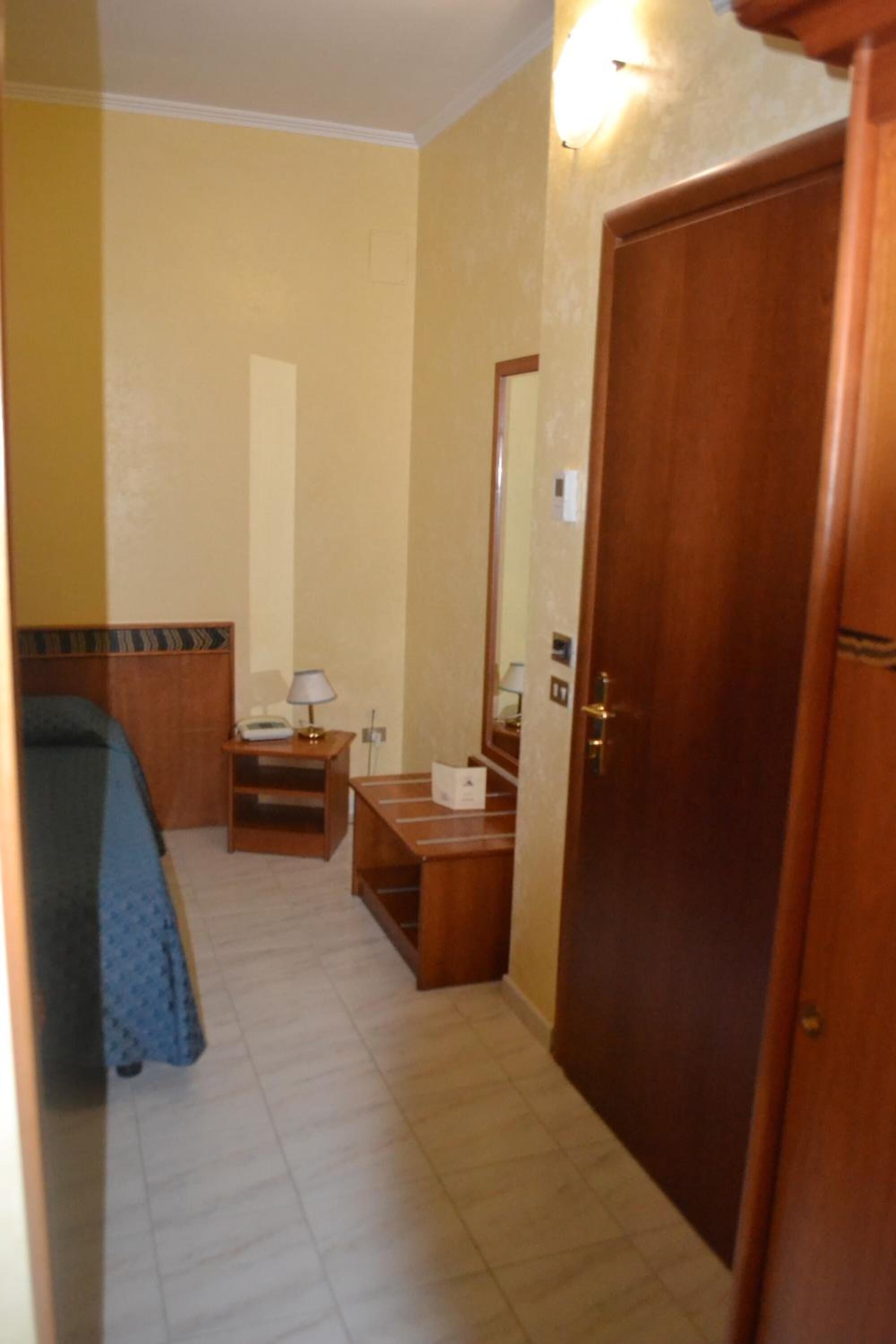 A hotel room with a bed, bedside table, lamp, and a wooden door.