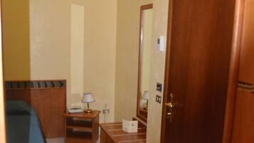 A hotel room with a bed, bedside table, lamp, and a wooden door.